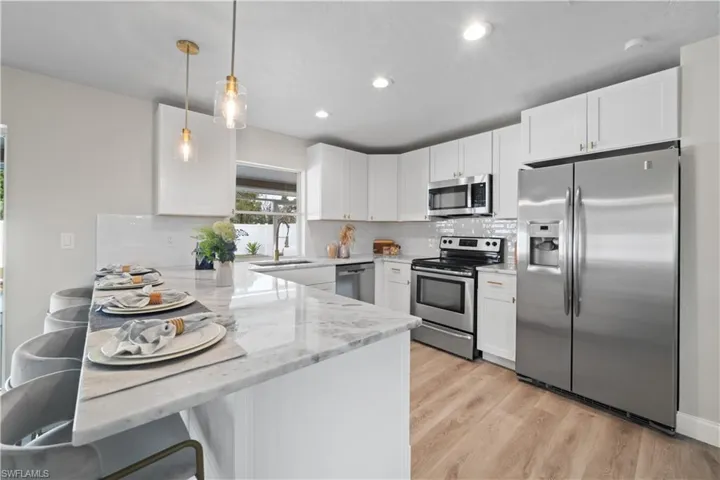 Kitchen featuring sink, white cabinets, light stone counters, kitchen peninsula, and appliances with stainless steel finishes