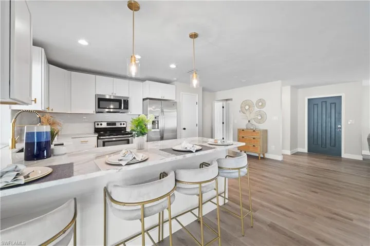 Kitchen featuring hanging light fixtures, decorative backsplash, white cabinets, appliances with stainless steel finishes, and a kitchen breakfast bar