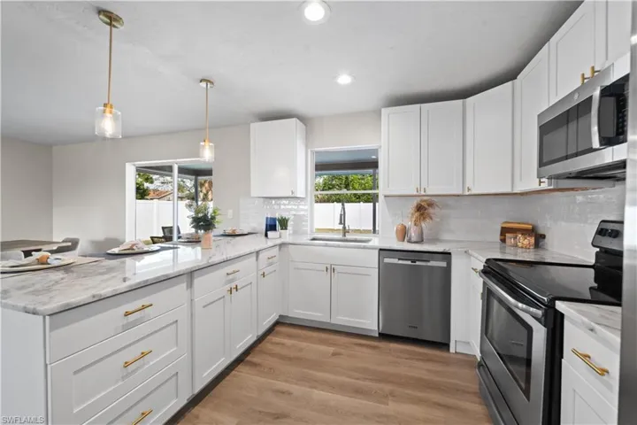 Kitchen with stainless steel appliances, white cabinets, hanging light fixtures, and sink