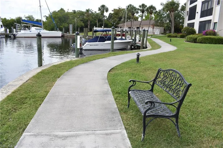 Waterfront pathway featuring a decorative metal bench and manicured lawn