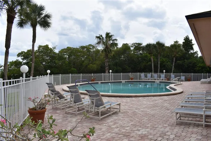 Outdoor swimming pool with a curved design, surrounded by a paver patio and a white aluminum fence