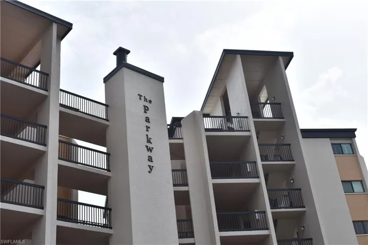 Multi-story building facade featuring numerous private balconies with dark railings, a prominent vertical signage element, and a contrasting dark roofline