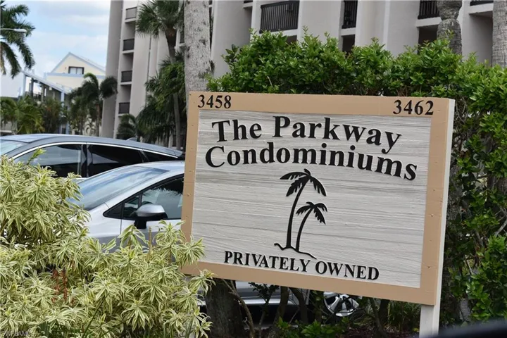 "The Parkway Condominiums" signage, featuring a palm tree graphic and numerical addresses 3458 and 3462, framed by green and variegated shrubs