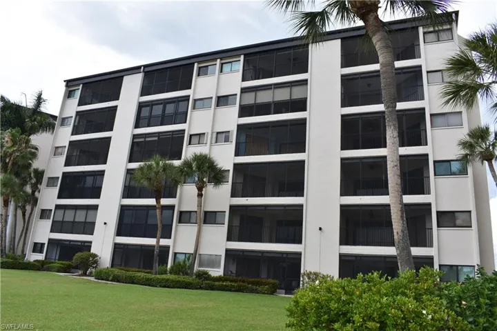 Multi-story building featuring white exterior, screened balconies, dark-framed windows, manicured lawn, and mature palm trees