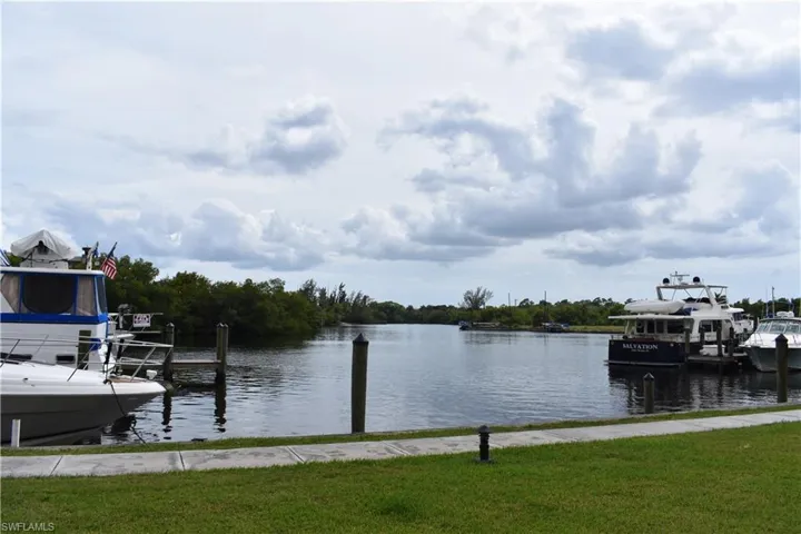 Waterfront setting featuring a navigable waterway, docked boats, and a manicured grassy area with a paved walkway