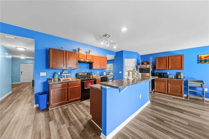 Kitchen featuring black appliances, a center island with sink, a breakfast bar, dark countertops, and brown cabinets