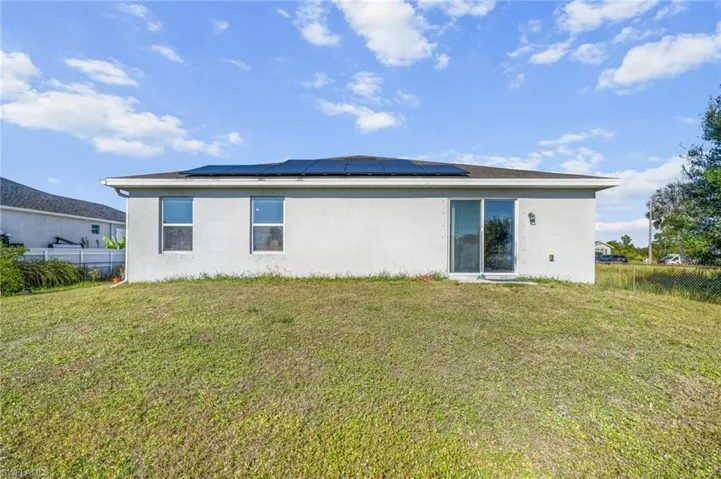 Rear view of property featuring stucco siding and solar panels