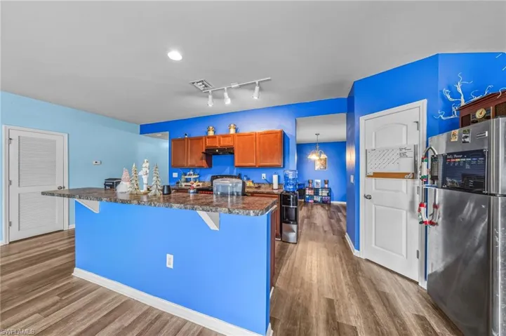 Kitchen featuring dark countertops, freestanding refrigerator, a kitchen breakfast bar, brown cabinetry, and dark wood-style floors
