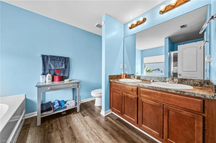 Full bath with a bath, double vanity, and dark wood-type flooring