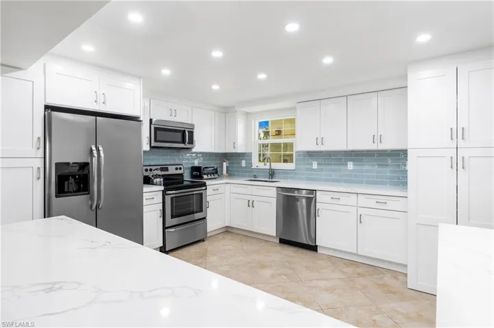 Kitchen featuring appliances with stainless steel finishes, white cabinets, light stone counters, and sink