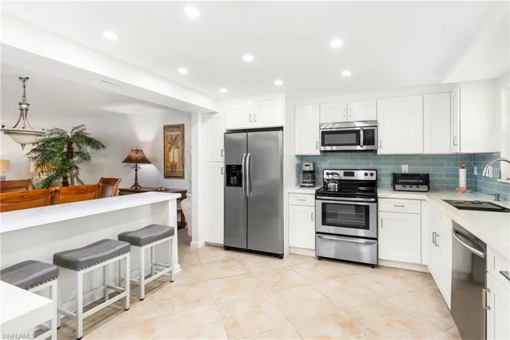 Kitchen with white cabinets, stainless steel appliances, decorative backsplash, sink, and light tile patterned floors