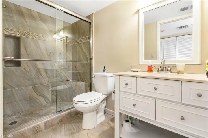 Bathroom featuring toilet, vanity, tile patterned flooring, and a shower with shower door