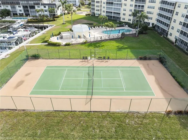 View of tennis court with a lawn and basketball hoop
