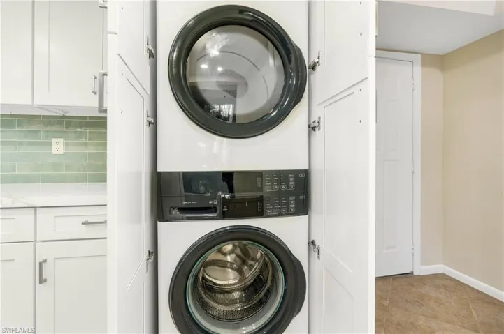 Clothes washing area with stacked washer / dryer and light tile patterned floors