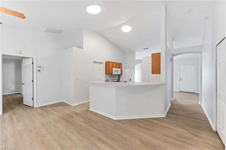 Kitchen featuring light wood-type flooring, white appliances, ceiling fan, kitchen peninsula, and high vaulted ceiling