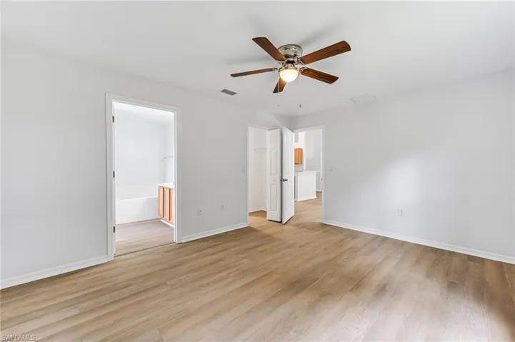 Unfurnished bedroom with light wood-type flooring, ensuite bathroom, and ceiling fan