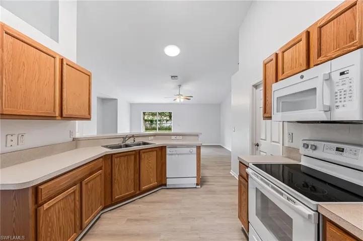 Kitchen featuring white appliances, light hardwood / wood-style floors, sink, ceiling fan, and a towering ceiling