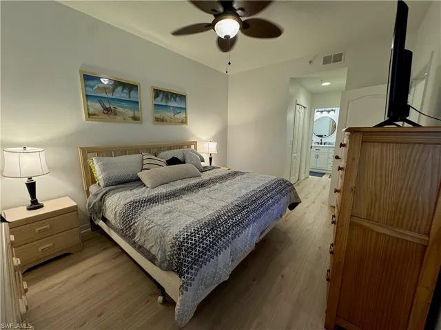 Bedroom with ensuite bath, light hardwood / wood-style floors, ceiling fan, and a closet