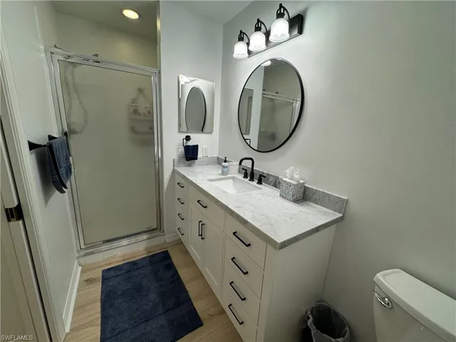 Bathroom featuring vanity, hardwood / wood-style flooring, toilet, and a shower with door
