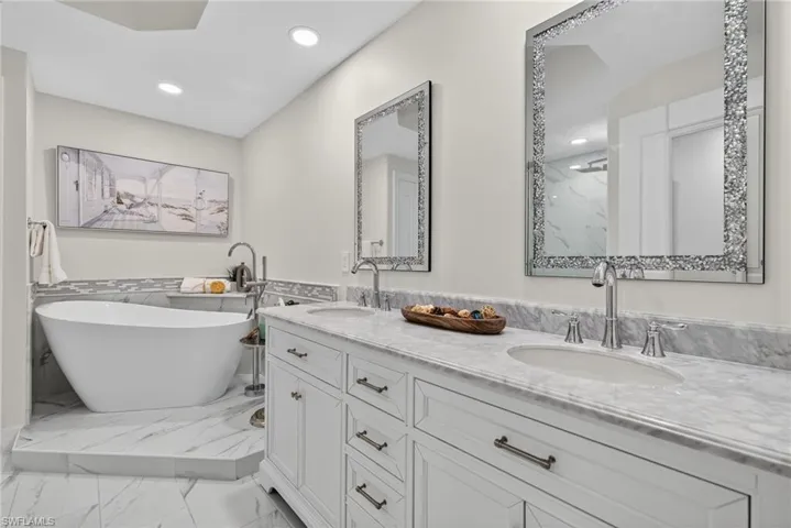 Bathroom featuring double vanity, light marble finish flooring, recessed lighting, a soaking tub, and a wainscoted wall
