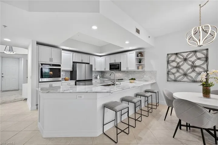 Kitchen with hanging light fixtures, open shelves, tasteful backsplash, appliances with stainless steel finishes, and light stone counters