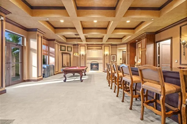 Recreation room with billiards table, beamed ceiling, coffered ceiling, ornamental molding, and a large fireplace