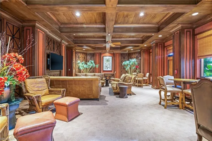 Living area with a wood ceiling with exposed beams, a ceiling fan, coffered ceiling, wooden walls, and ornamental molding