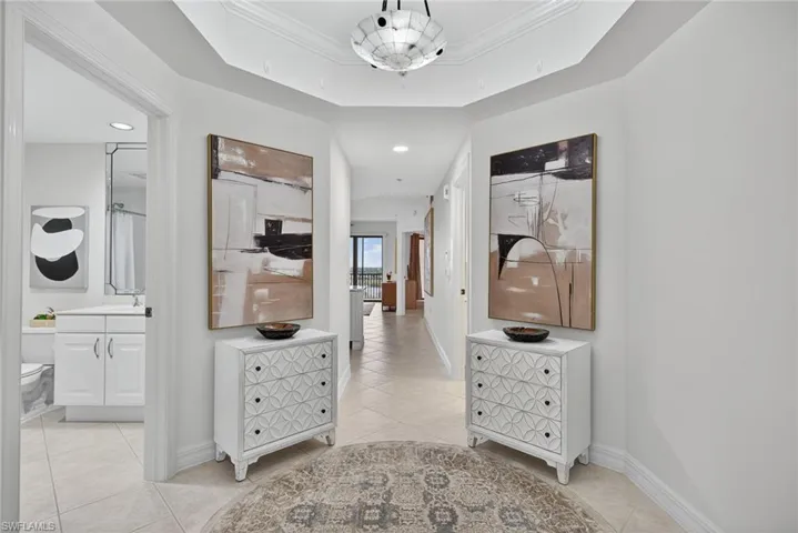 Hall with a tray ceiling, light tile patterned floors, crown molding, and recessed lighting