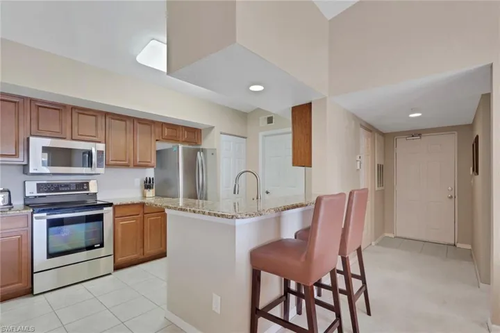 Kitchen with a breakfast bar area, stainless steel appliances, wood finish cabinets, and light stone countertops