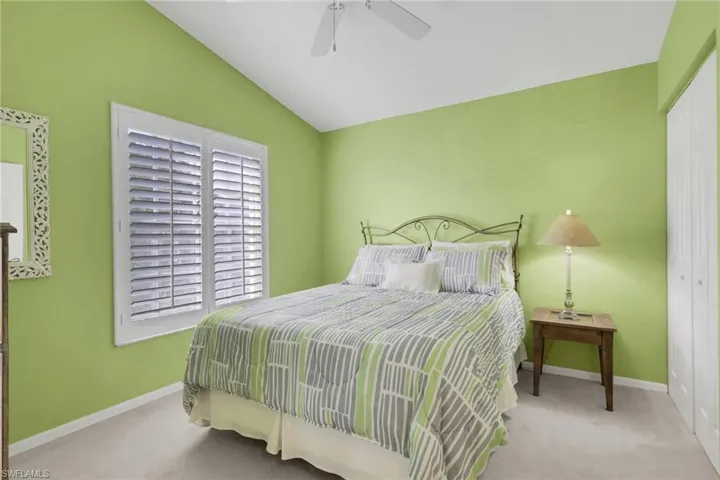 Bedroom featuring  plantation shutters, walk in closet, light colored carpet,  and a ceiling fan
