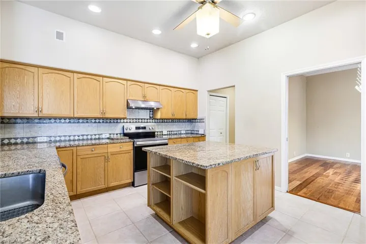 Kitchen with a kitchen island, ceiling fan, Granite counters, light tile floors, and Newer Stainless Steel Appliances