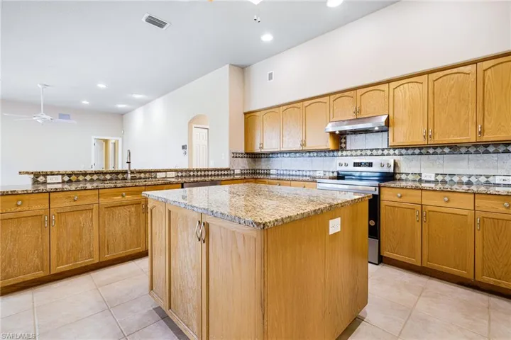 Kitchen with a kitchen island, ceiling fan, Granite counters, light tile floors, and Newer Stainless Steel Appliances