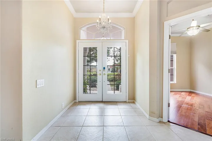 Entryway featuring ornamental molding, an inviting chandelier, light tile flooring, and french doors