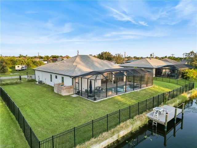 Back of property with a dock overlooking the water a patio, a lawn, and a lanai.