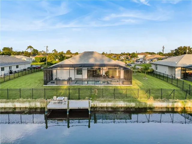 Back of property featuring a canal view with a dock, an expansive lanai, a pool and spa.