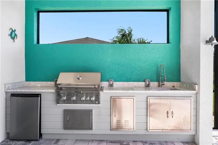 Outdoor kitchen with grill, mini fridge and sink area.