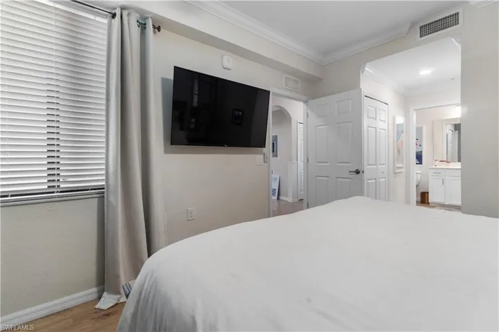 Bedroom featuring a closet, connected bathroom, hardwood / wood-style flooring, and crown molding