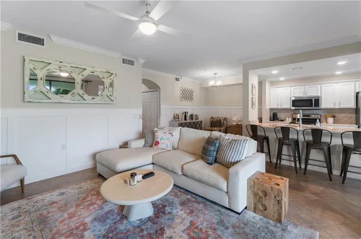 Living room featuring dark tile patterned floors, ceiling fan with notable chandelier, and crown molding