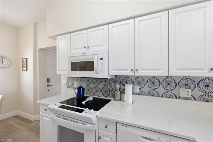 Kitchen featuring white shaker-style cabinetry, patterned tile backsplash, quartz countertops, and built-in appliances