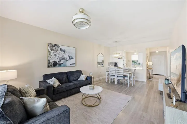 Open-concept main living area featuring light-toned wood-finish flooring, a contemporary drum-style ceiling light fixture, and a kitchen pass-through window with an integrated dining counter