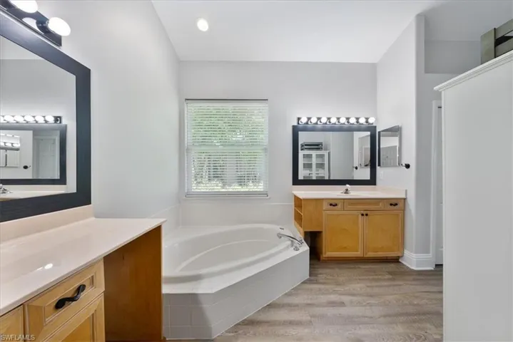 Bathroom featuring double vanity, tiled bath, and wood-type flooring