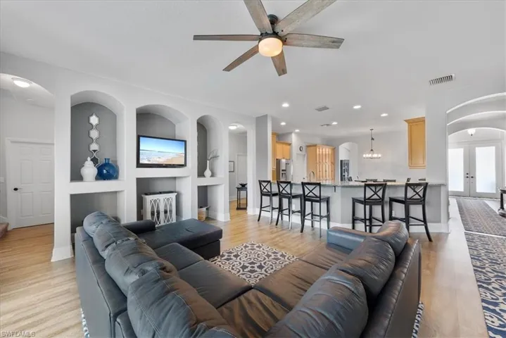 Living room with ceiling fan with notable chandelier, light hardwood / wood-style flooring, built in shelves, and french doors