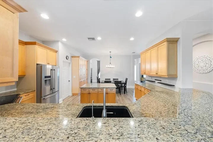 Kitchen with stainless steel refrigerator with ice dispenser, light hardwood / wood-style flooring, a kitchen island, hanging light fixtures, and light stone countertops