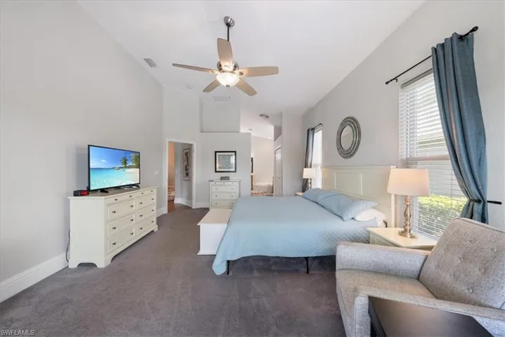 Bedroom with high vaulted ceiling, connected bathroom, dark colored carpet, and ceiling fan