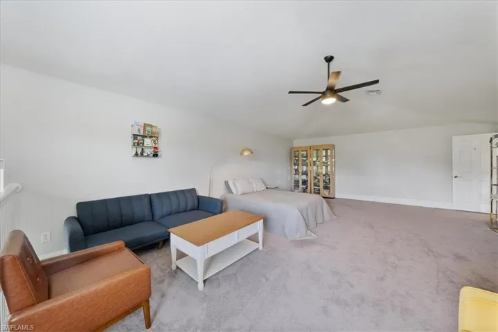 Carpeted living room with ceiling fan and vaulted ceiling