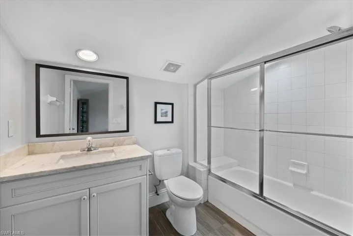 Full bathroom with vanity with extensive cabinet space, hardwood / wood-style floors, toilet, and bath / shower combo with glass door