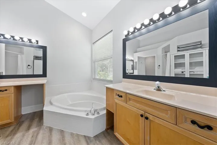 Bathroom with hardwood / wood-style flooring, lofted ceiling, tiled tub, and vanity
