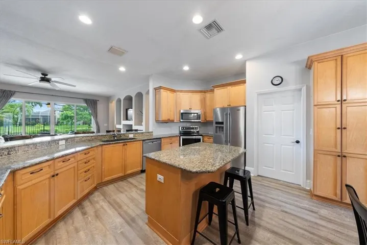 Kitchen with appliances with stainless steel finishes, ceiling fan, light hardwood / wood-style flooring, and a kitchen island