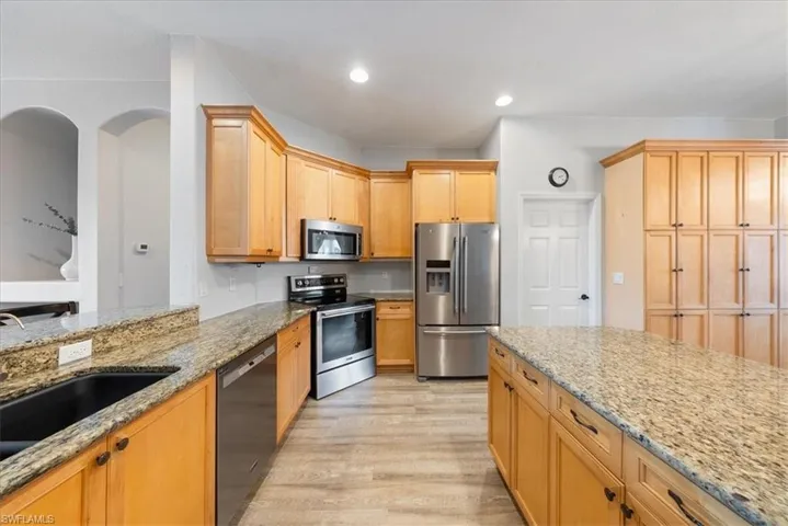 Kitchen featuring light stone countertops, sink, light wood-type flooring, and appliances with stainless steel finishes