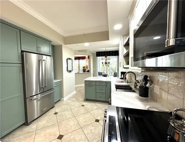Kitchen with appliances with stainless steel finishes, hanging light fixtures, backsplash, and green cabinetry